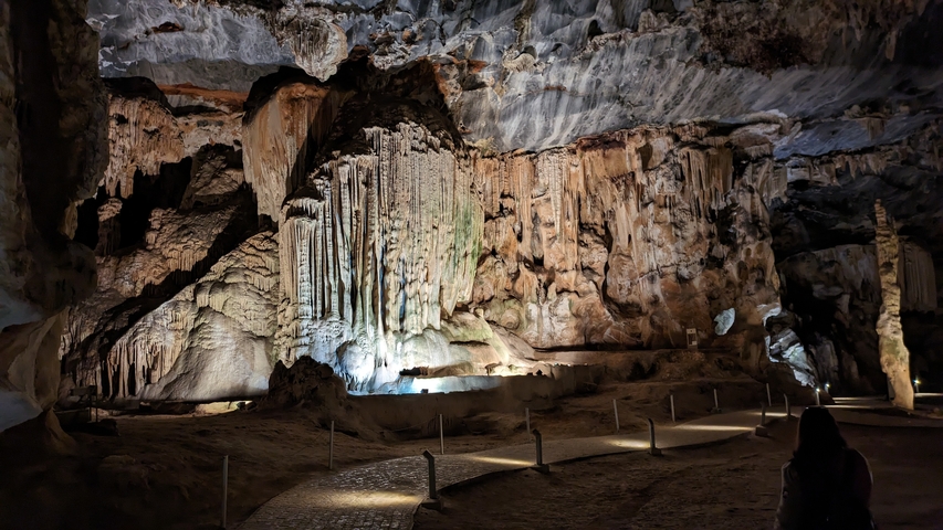      A large cave with beautiful rock formations inside, dimly lit with pathways.
  