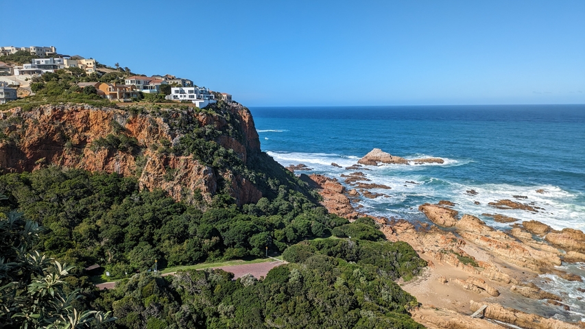 A scenic view of rocky coastline with waves crashing against the rocks, under a blue sky.