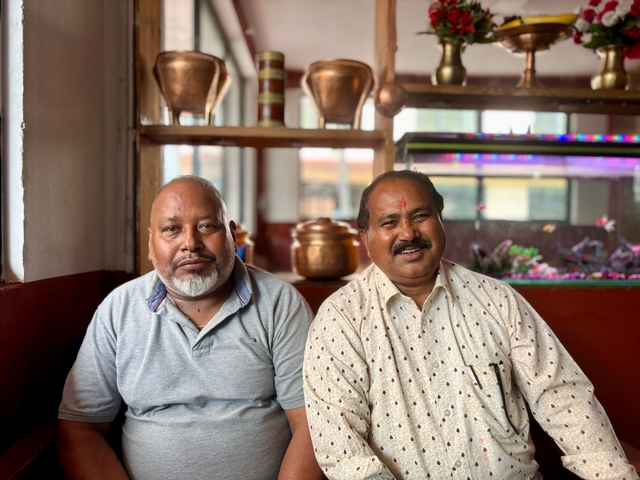       Two men posing inside a restaurant with decorative pots.
  