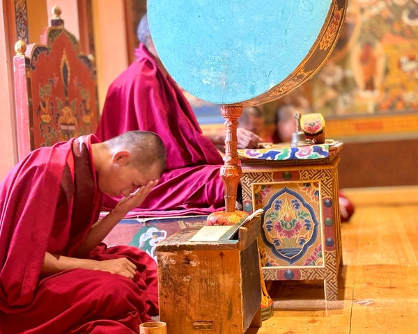       Monks in traditional robes inside a monastery, one bowing in prayer.
  