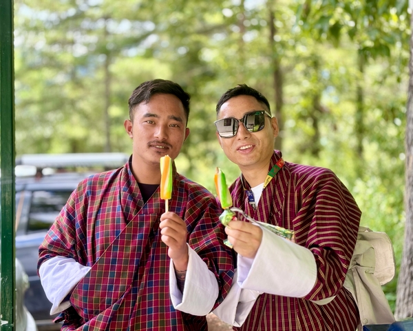       Two men in traditional Bhutanese dress smiling with ice cream.
  