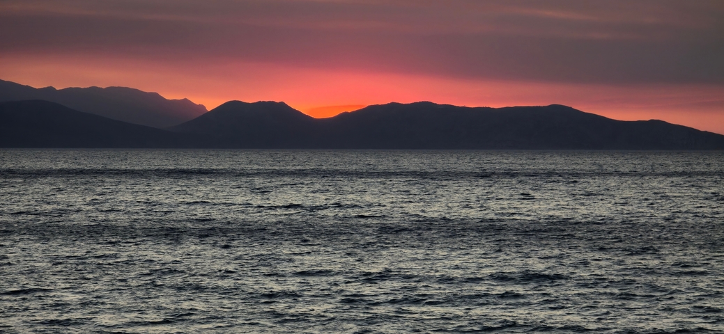 Ocean view with a dramatic sunset over distant mountains.