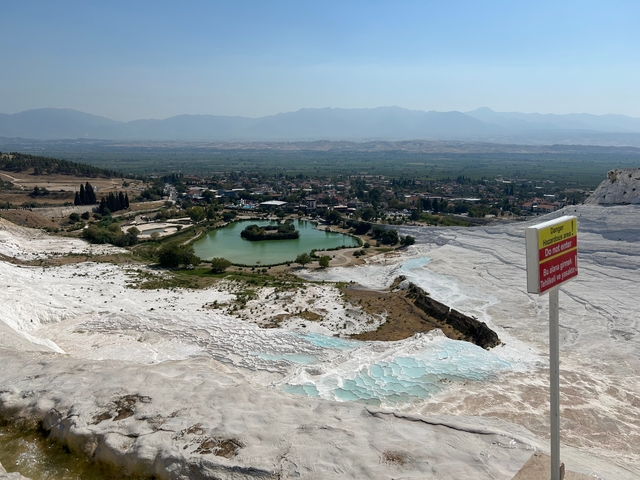 Aerial view of Pamukkale terraced limestone formations with pools and a distant city view.