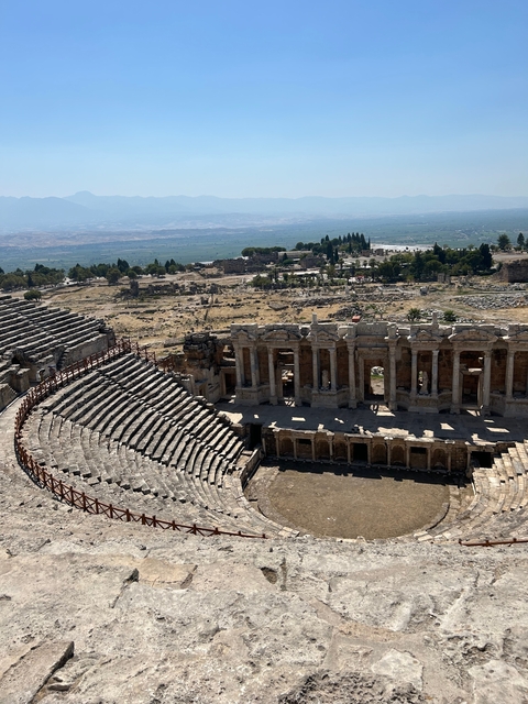 Ancient Roman amphitheater with surrounding ruins and distant landscape.