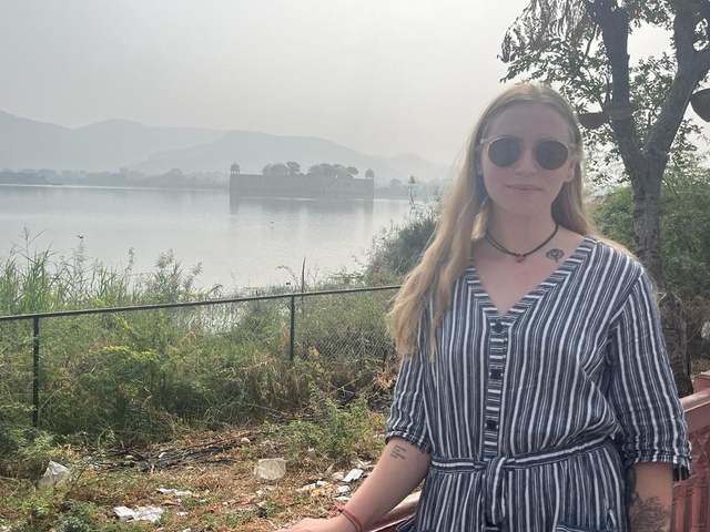 Woman in sunglasses near a lake with a distant palace.