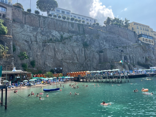 Beach with people and umbrellas under a cliff.