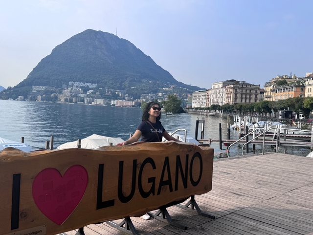       Person holding a 'I love Lugano' sign by the lake.
  