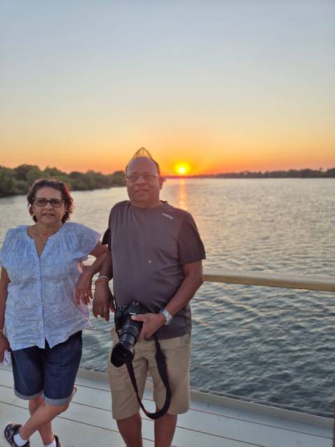      Two people standing by a river during sunset.
  