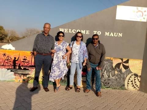       Four people standing in front of a wall with a 'Welcome to Maun' sign.
  