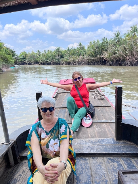       Two women posing on a traditional boat in a forested river.
  