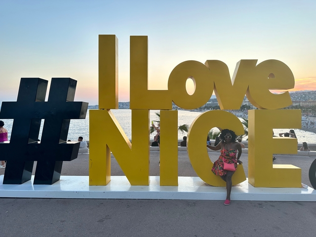 Person sitting in front of 'I Love Nice' sign by the water.