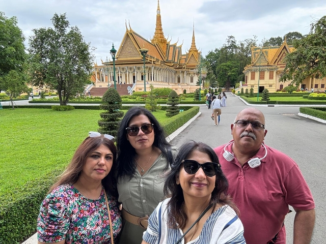       Four people posing in front of a historic building with gardens.
  