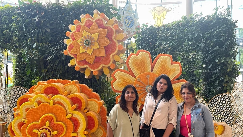       Three women posing in front of decorative floral displays.
  