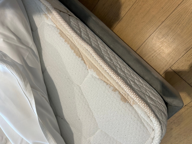 Edge of a stained mattress on a wooden floor.