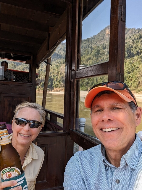      Couple taking a selfie on a wooden boat along a river.
  