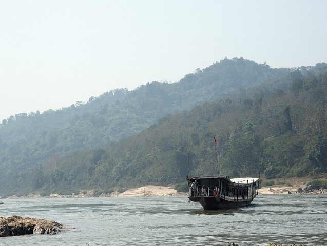       Boat on a river with a backdrop of green forested hills.
  