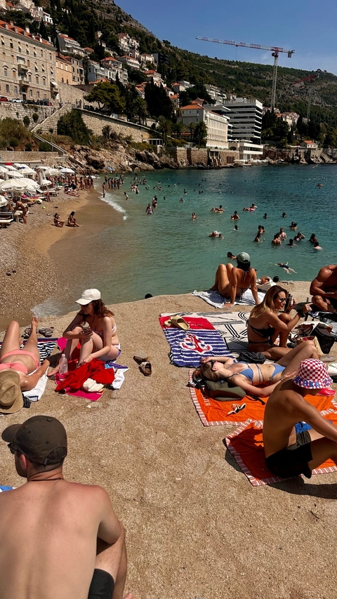 People sunbathing and swimming at a crowded beach.