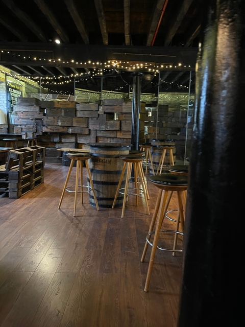       Interior of a rustic bar with wooden barrels and stools.
  