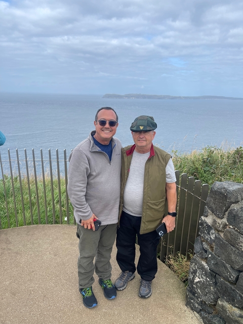       Two people posing by an ocean overlook with fencing.
  