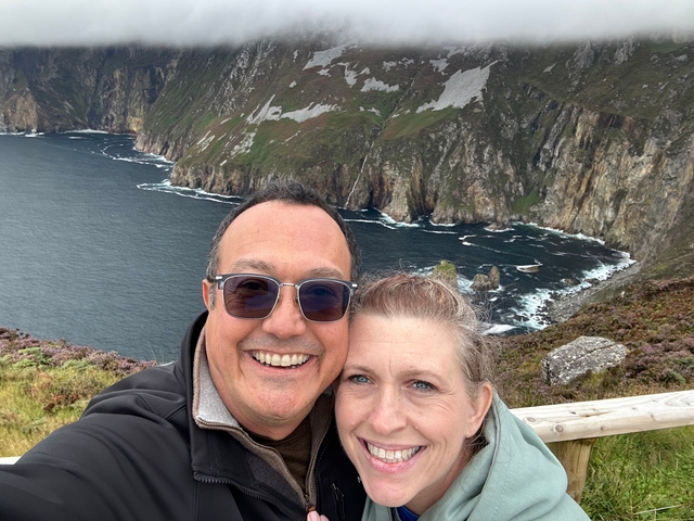 Couple posing in front of a coastal view with cliffs.