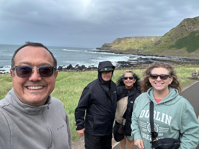 Group of people standing along a coastal path in windy weather.