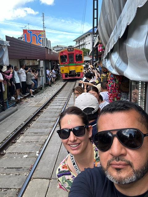       People taking photos of a train passing through a busy market.
  