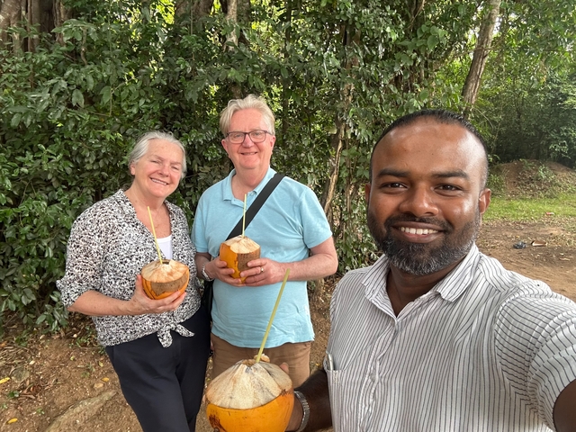 Three people posing with coconuts in an outdoor setting.