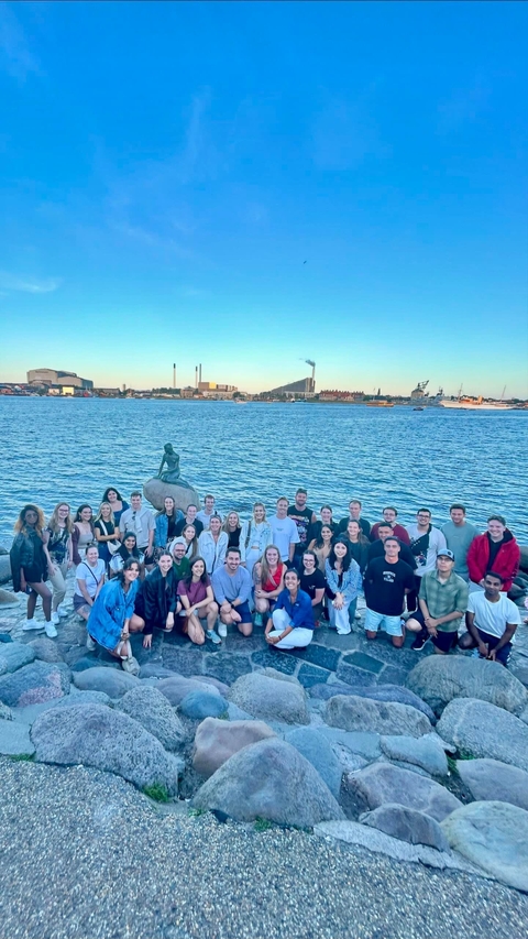       Large group posing with a waterfront and cityscape behind.
  