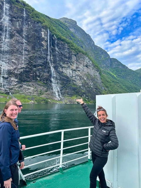       People on a boat with a scenic waterfall in the background.
  