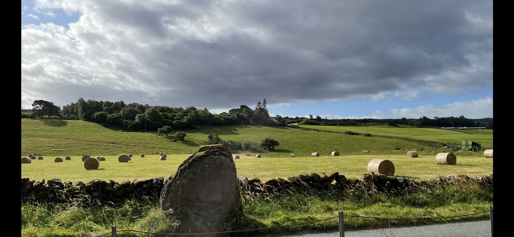 Open field with hay bales and a cloudy sky.