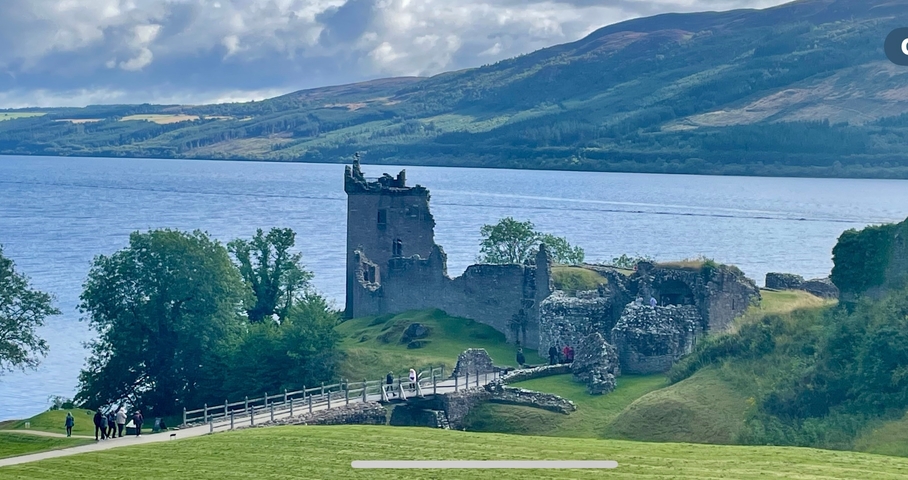       Ruins of a castle by a lake with hills in the background.
  