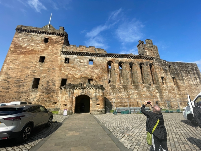       Tourist taking photo of a historical building with cars parked nearby.
  