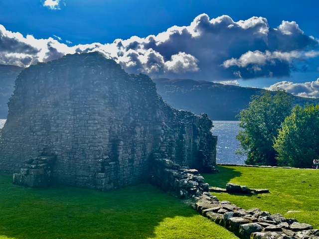 Ruined stone structure by a lake with mountains in the background.