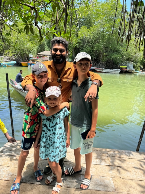 Group of people posing near boats in a river setting.
