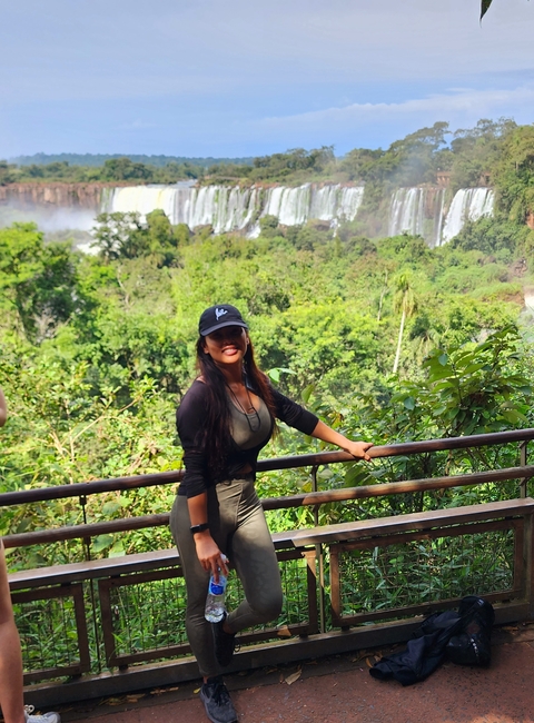 Person smiling in tropical surroundings with waterfalls blurred in the distant background.