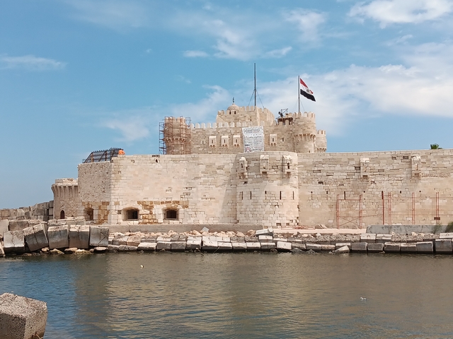 A historic fort with an Egyptian flag, by the water.