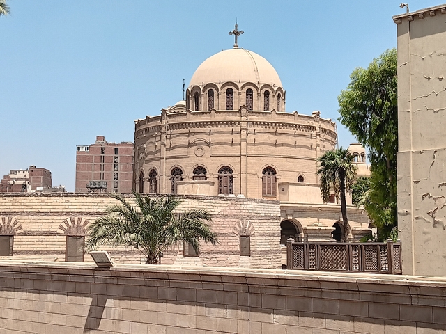       A large domed building surrounded by palm trees under a clear sky.
  