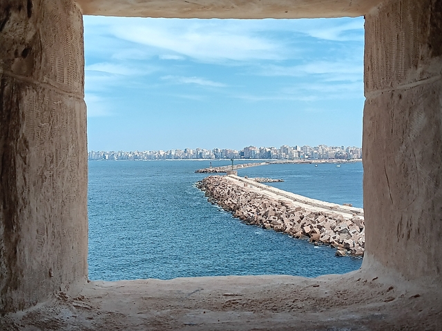 View through a stone window of the sea and distant city skyline.