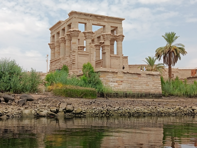 Ancient temple structure near the Nile River, partially surrounded by greenery.