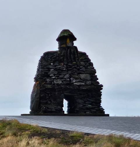       Stone statue resembling a man under a cloudy sky.
  
