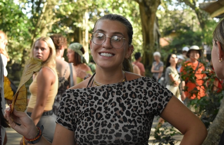 Smiling woman holding a leaf with a group of people in the background.
