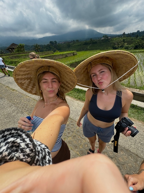 Two women wearing large hats, posing for a selfie outdoors.