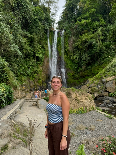 Woman posing near a waterfall with lush greenery.