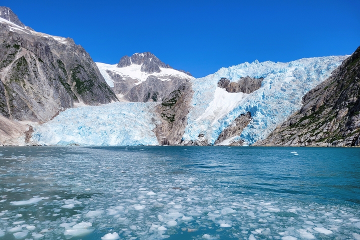 A large glacier with icy blue tones near a body of water.