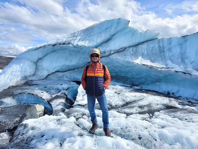       Person standing in front of a massive glacier.
  