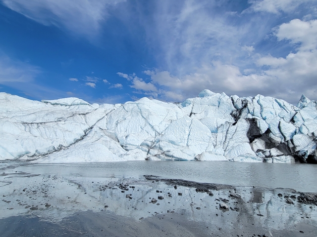       Panoramic view of a glacier reflecting in calm water.
  