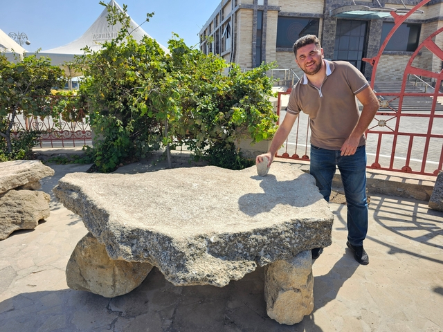 A man posing with his hand on a large stone table.