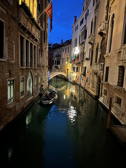       A gondola floating in a narrow canal flanked by historic buildings at night.
  