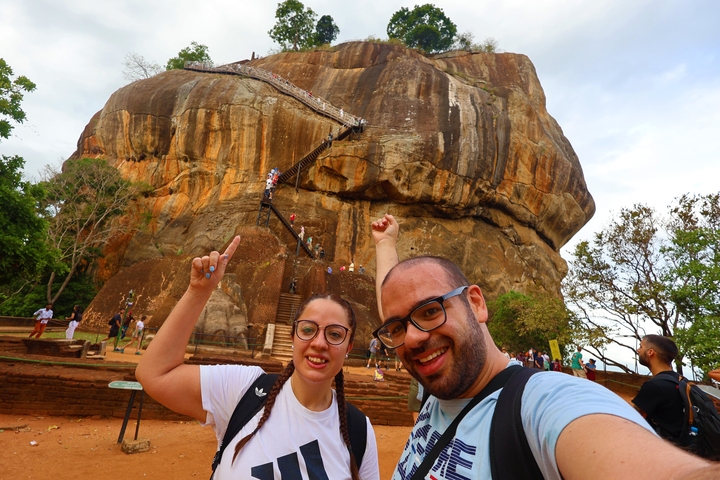 Two people posing in front of a massive rock formation with stairs.