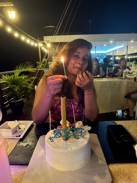       A woman holding a lit candle at a dining table, surrounded by people.
  